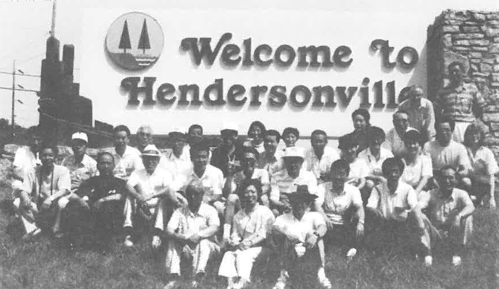 A group sits in front of the welcome to Hendersonville sign